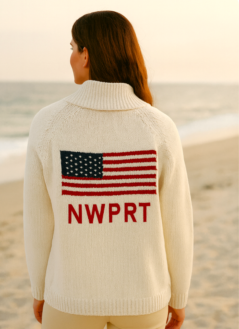 Person wearing a cream sweater with an American flag and 'NWPRT' text on a beach.